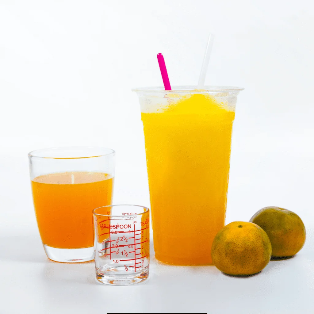 A glass of Sonic Orange Cloudsicle Slush Float with an orange glass and a measuring cup beside and two oranges rested on the side
