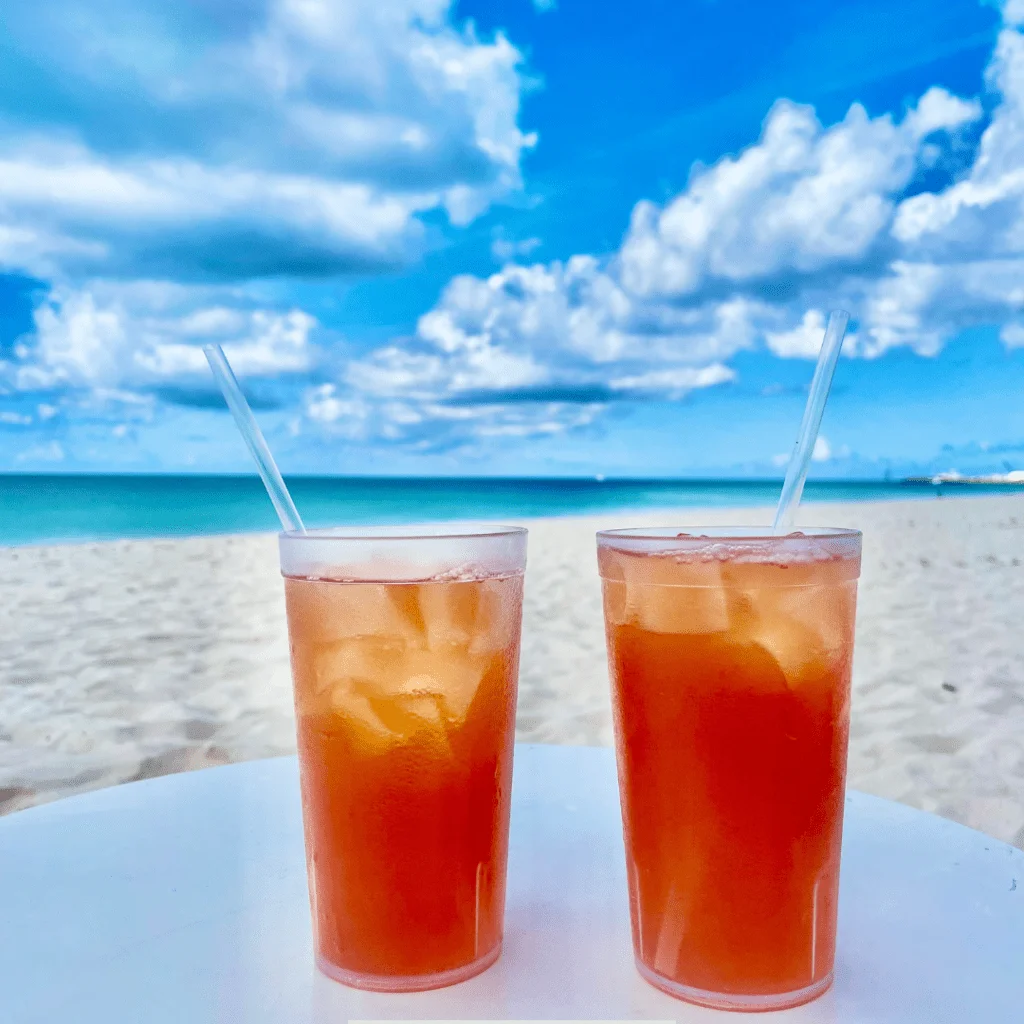 two glasses of Calico Jack Rum Punch with a beautiful sunset color, topped with a twisted peel of orange, served on a beach