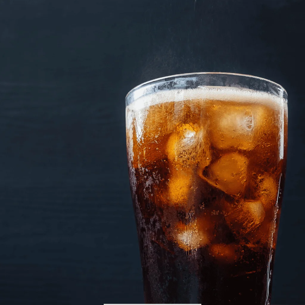A glass of chilled copycat homemade olipop fizzing on top and served with ice in it on a black background