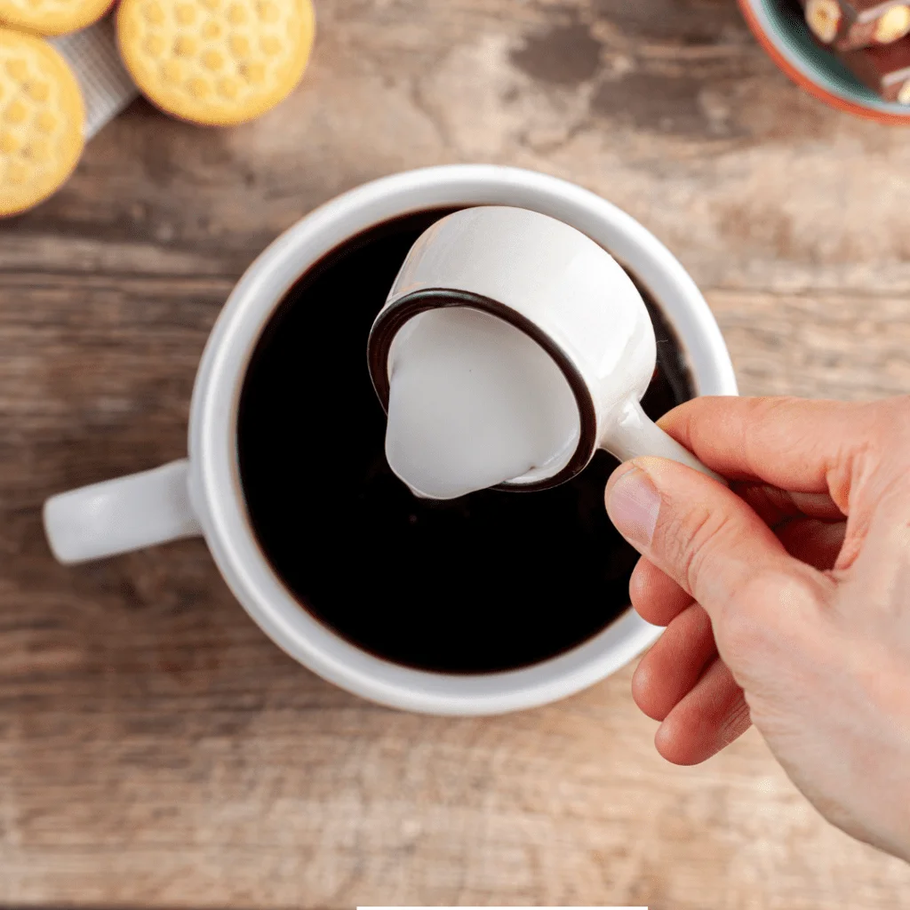 Creamer being poured from a small cup into a mug of black coffee